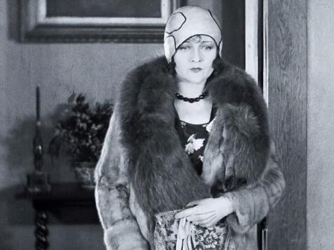 Actress Isabel McDonagh (billed as Marie Lorraine) in a scene from the cheaters. She is pictured wearing a fur coat and a hat.