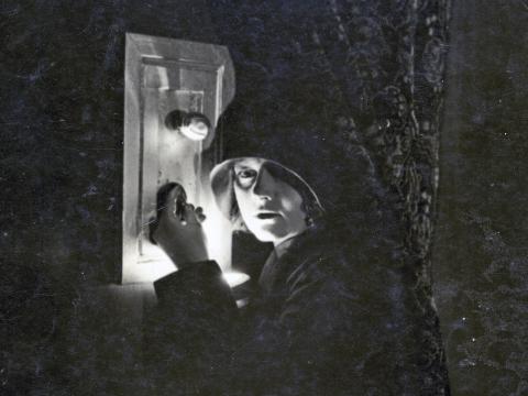 Actress Isabel McDonagh (billed as Marie Lorraine) in a scene from the cheaters. She is pictured wearing a dark hat and coat and trying to break into a safe in the darkness. 