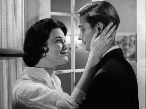 A woman gazes into a man's eyes with her hand touching the back of his head
