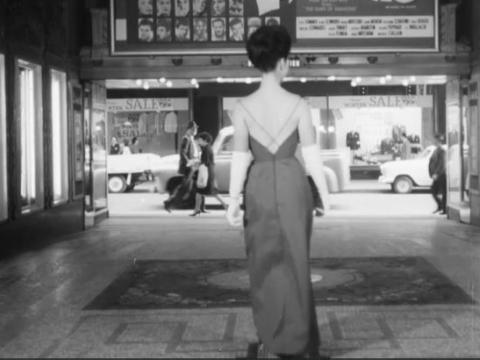 Woman in an evening gown standing the foyer of a theatre.