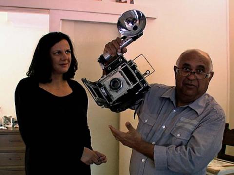 Photojournalist Mervyn Bishop holds up a camera and flash while being interviewed by presenter Hetti Perkins