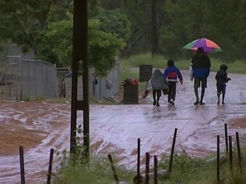 A shot from behind of Aboriginal people walking through the rain holding an umbrella