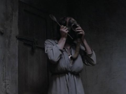 Nicholas Hope as Bubby dressed in women's clothing holding a gas mask to his face