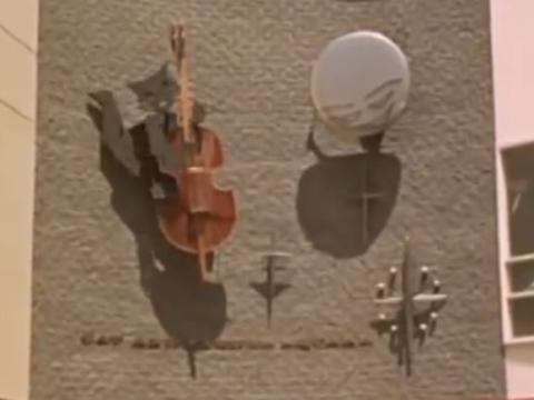 A clock on the wall of a building with a moving sculpture of a cat playing a fiddle and a cow jumping over a moon. 