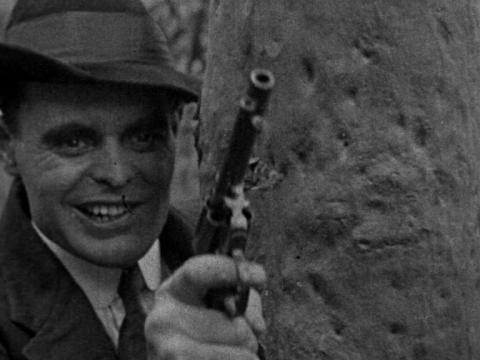 Gang bos Bill Warne (Billy Ryan) behind a tree holding a gun