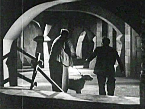 George (George Wallace), Henry (John Dobbie) and their dog Aloysius with backs to camera enter a dark haunted house
