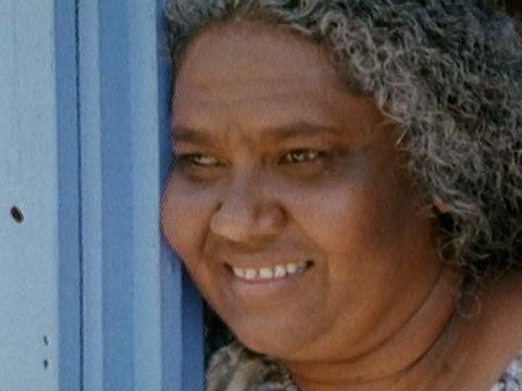 Gilladi (Sylvia Clarke) leaning against a door and smiling