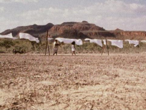 Wide shot of older and younger Aboriginal women walking along a line of white sheets on a line