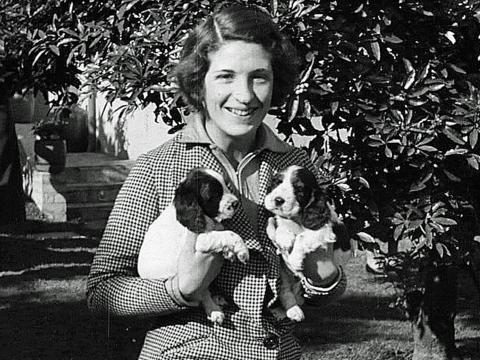 A young woman holds 2 cocker spaniel puppies, circa 1930