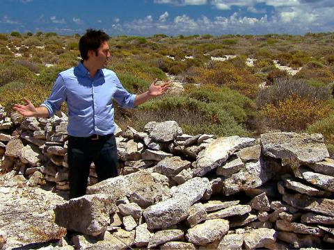 Man standing at an archaeological site of piled stone.