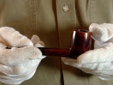 Close up of hands wearing gloves and holding a pipe.