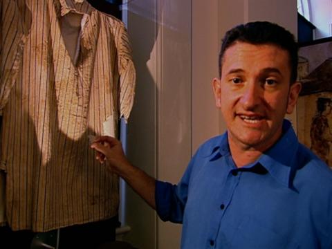 Warren Brown stands next to a convict shirt in a museum display.