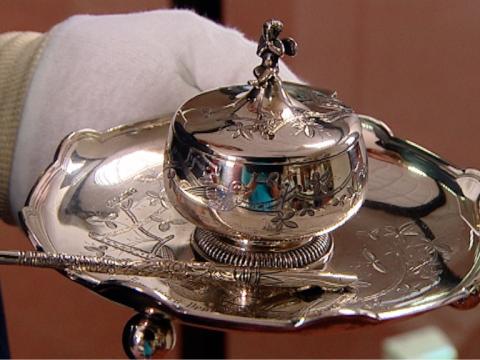 Close up of a gloved hand holding a silver ink stand on a tray.