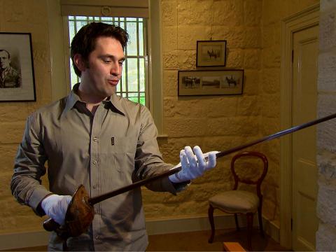 Man wearing whote gloves holding Francis de Groot's sword.