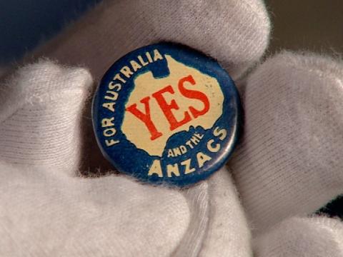 Close up of a gloved hand holding a small metal badge with the words 'For Australia and the Anzacs' and a map of Australia with the word 'Yes' in red in the centre.