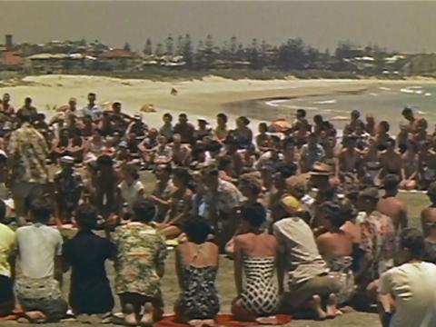 A large crowd of people kneeling in a circle at the beach