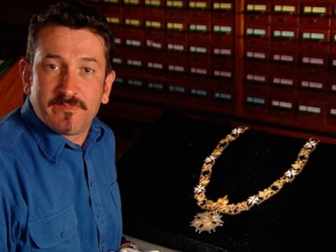 Warren Brown stands next to a display of an elaborate necklace and pendant.