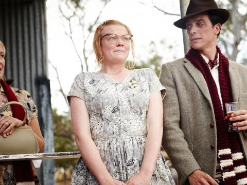 Sarah Snook as her character Gertrude in The Dressmaker. She is looking frumpy in glasses and a floral frock, standing next to James Mackay (William). On the other side, slight cut out of frame is Rebecca Gibney who plays Gertrude's mother Muriel.
