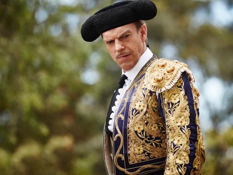 Hugo Weaving in a scene from The Dressmaker. He's photographed from the waist up wearing an embroidered navy blue and gold matador jacket and black matador hat.