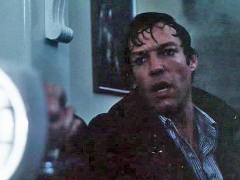 A wet and frightened man holding a flashlight.
