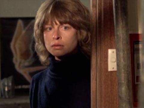 A woman looks scared peering around a door