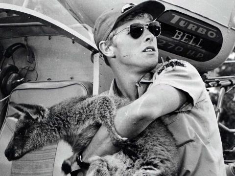 Helicopter pilot Tony Bonner carries Skippy in his arms, with his helicopter visible in the background