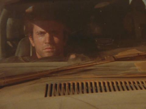 Mel Gibson as Mad Max driving a car