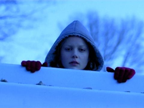 A woman is looking over a wall. She is wearing woollen gloves.