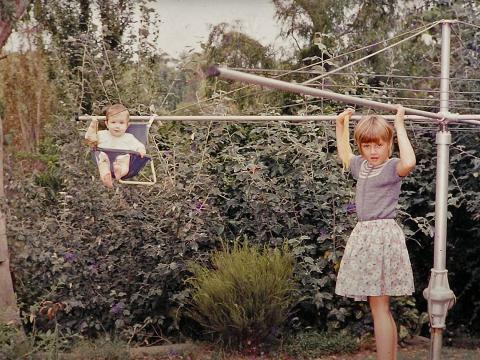 Two kids playing on a hills hoist clothesline.