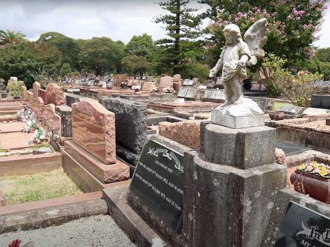 Rows of headstones in a cemetery. The one in the foreground has an angel on top.