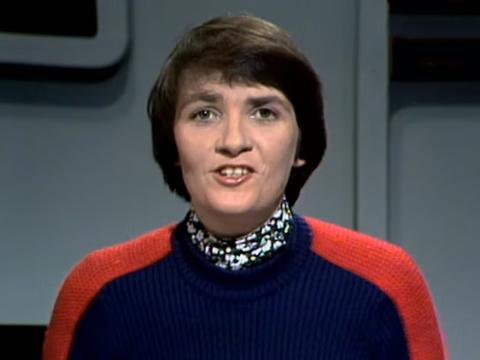 Head and shoulders shot of a woman sitting in a TV studio presenting news.