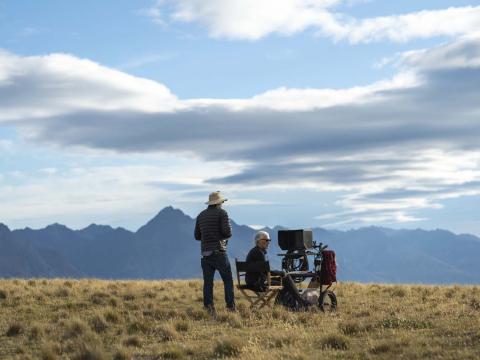 Cinematographer Ari Wegner standing next to director Jane Campion, seated at a monitor, on a grassy mountain location in New Zealand for the movie The Power of the Dog