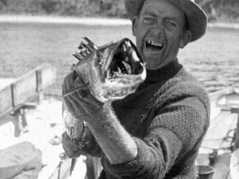 A man laughs as he holds a dead barracouta fish.