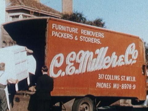 A truck with a red side and in white writing C.E. Miller & Co, two men taking furniture off the back