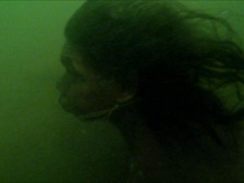 Burrimmilla (David Gulpilil) swims beneath the water. The water has a green tinge.