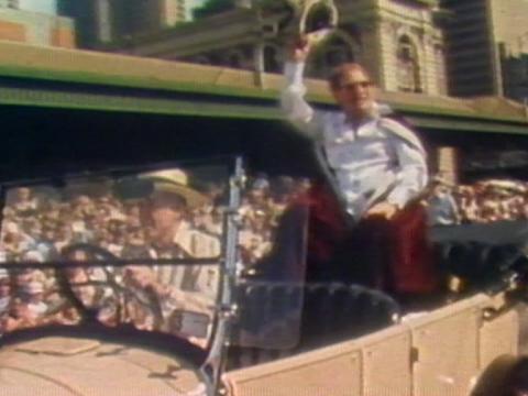 Graham Kennedy in the back of a convertible waving to the crowds as King of Moomba