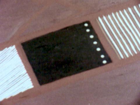 Close-up of an Aboriginal bark painting. The colours are ocre, white and black with stripes and dot shapes.