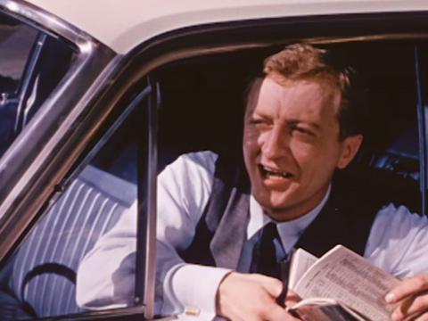 Graham Kennedy leaning out of a car window asking for directions 