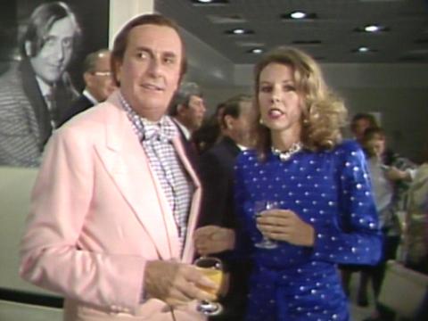 Barry Humphries is wearing a pink suit jacket with his hair slicked back. Diane Milstead is standing next to him. 