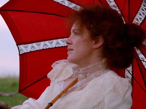 Actress Judy Davis in a scene from My Brilliant Career. Pictured in close up from the shoulders up in a lace dress, she is reclining under a bright red parasol.