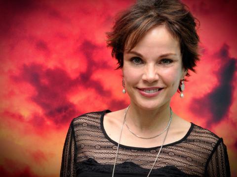 Head and shoulders close up of actress Sigrid Thornton in front of an orange background. 