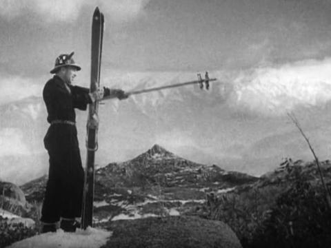 A man stands on a snow-covered hill with skis and points with his stocks