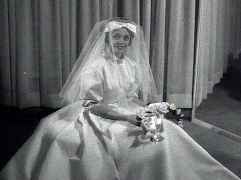 Woman wears a volumous wedding gown complete with veil and bow.