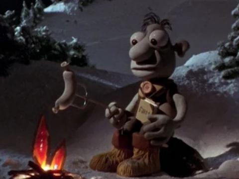 Animation still of a goofy looking man cooking a sausage over a camp fire.