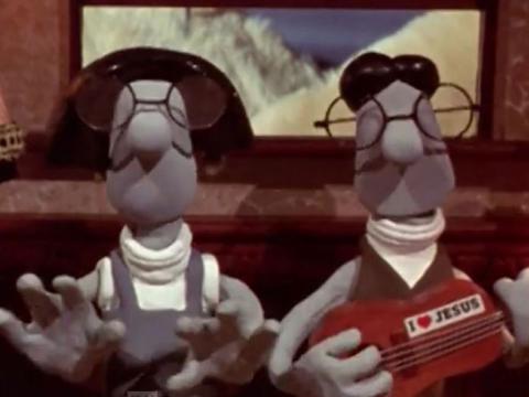Animation still of two characters, both wearing oversized glasses and one playing a guitar with a sticker that reads,'I heart Jesus'.