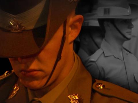 An Anzac soldier in slouch hat stands with bowed head while another Anzac soldier is marching behind him