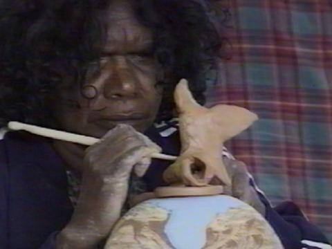 Close up of an Indigenous woman working on a piece of pottery.