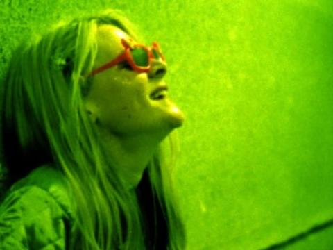 A young woman is laughing in green neon light. She is wearing red kid's sunglasses.