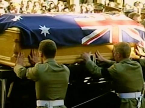 Two uniformed soldiers attaching an Australian flag to a coffin at a state funeral