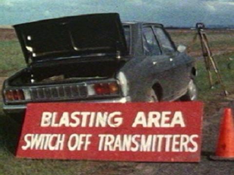 Car on the side of road with its boot open and a sign that reads 'Blasting Area. Turn off transmitters'.